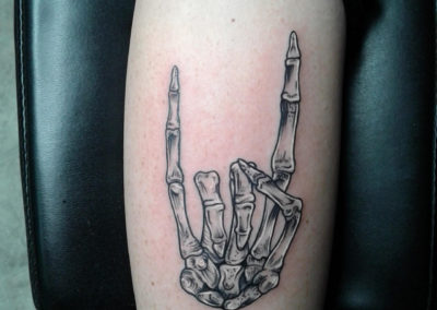 A black and white tattoo of a skeleton hand with horns.