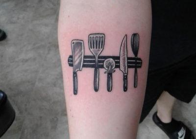 A black and white tattoo of kitchen utensils