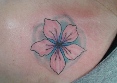 A pink flower with blue center tattoo on the back of a woman 's shoulder.
