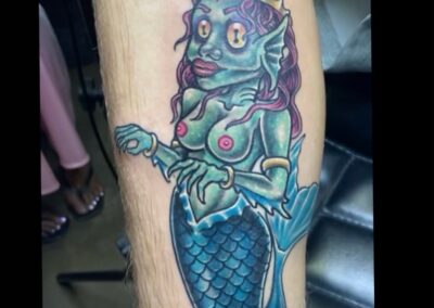 A tattoo of a green creature sitting on top of a blue fish.