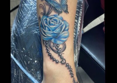 A blue rose tattoo with a rosary and butterfly.