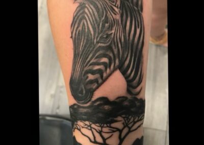 A zebra tattoo with trees and a tree trunk.