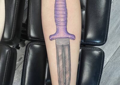 A purple knife tattoo on the arm of someone.