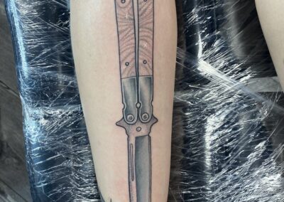 A tattoo of a knife with a spider on it.