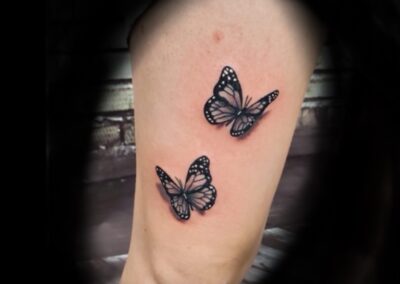 A pair of butterflies are sitting on the side of a woman 's foot.